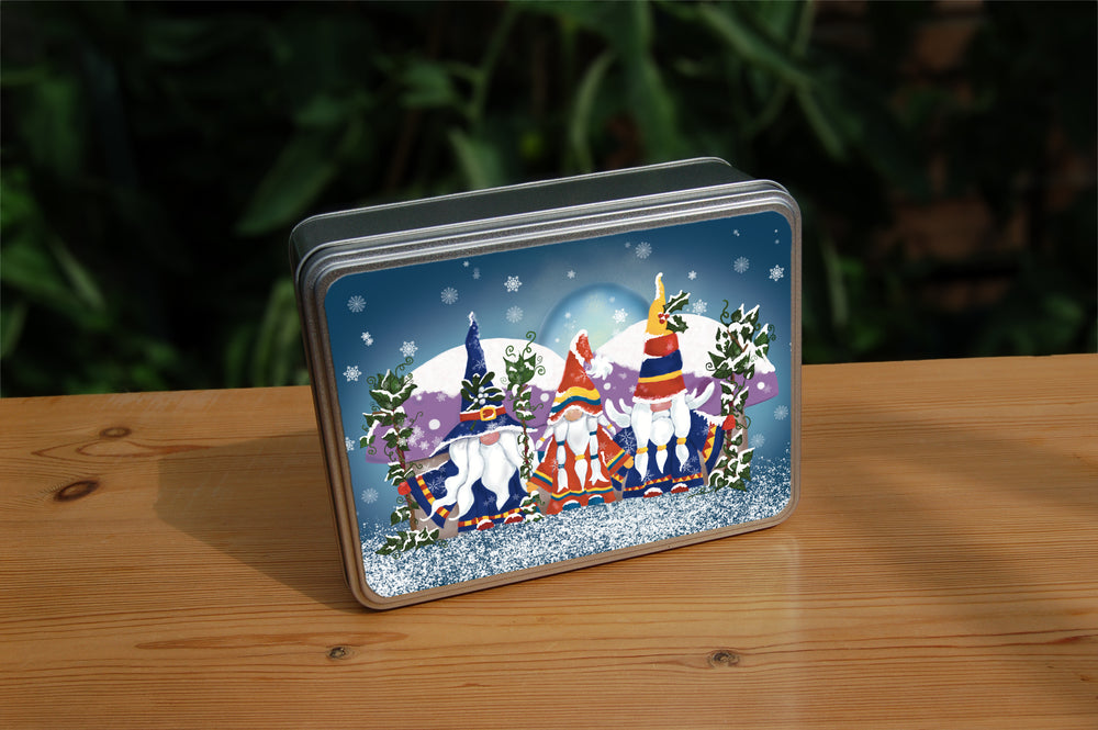 Three simple and colourful gnomes standing side by side. Only their round noses are visible as they all have long white beards and hair reaching nearly to their feet, and large hats pulled down over their eyes. The middle gnome is dressed in a red coat and hat, the outer two in dark blue. All are partially covered in snow and all carry an ivy-covered staff. Behind them are two large purple toadstools. Snow is falling and lies on the ground in front of them.