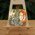 A woodland scene. On the left is a badger, sitting against a moss-covered tree trunk in the centre of the image, looking towards a crouching woman with bright red hair, her bare arms folded across her chest with her hands over her shoulders. She looks towards the badger with eyes part-closed. Blackberries hang above the badger, with autumn leaves and mushrooms at its feet. The woman is surrounded by large, autumn coloured leaves, with blackberries at her knees. Overall colours are oranges, reds and greens.
