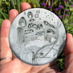 Black and white pencil drawing of a raised oval-shaped corner bed where the walls are carved out in random shapes to make pocket shelves containing plants, bottles, animal skulls and books. A blanket hangs over the side, and a spider sits in the tendrils of a vine wrapped around the foot of the bed. A string of charms including a key, spider, bottle, moon and feather is strung above the bed and a spider web has been spun in the corner.
