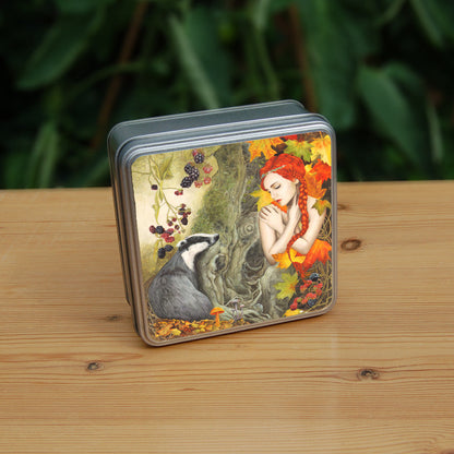 A woodland scene. On the left is a badger, sitting against a moss-covered tree trunk in the centre of the image, looking towards a crouching woman with bright red hair, her bare arms folded across her chest with her hands over her shoulders. She looks towards the badger with eyes part-closed. Blackberries hang above the badger, with autumn leaves and mushrooms at its feet. The woman is surrounded by large, autumn coloured leaves, with blackberries at her knees. Overall colours are oranges, reds and greens.