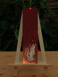 A naked, pale gold coloured, human-shaped angel falls front-first. Her arms, legs and wings are stretched back and up, and she's losing a few feathers. She appears to be falling towards flames, which are down below the level of the design. The background is mid-orange at the bottom, progressing towards very dark orange at the top.