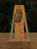 Rectangular bookmark: A compact-shaped owl with brown feathers sits sideways on an upright, roughly semi-circular stone arch, while looking directly at the viewer. The arch is decorated with a central circular Celtic knotwork design. The design is mostly monochrome apart from the owl, with a background of mottled dark tan.