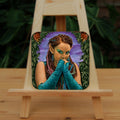 A brown-skinned female elf with long braided brown hair tied back, looks toward the viewer, hands held together in front of her mouth as though to suppress laughter. She wears a turquoise sleeveless dress and elbow-length arm sleeves. She's surrounded by ivy with a butterfly in each corner.