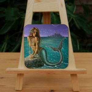 A mermaid leans on a rock, using her arms to hold herself clear of the water. She's on the shoreline, and is looking over her shoulder, across the teal-coloured sea, towards a rocky island with tall, pointed buildings on top. The sky is purple, and a crescent moon and flying seabirds are visible. The mermaid is naked with a teal fish tail, curled up towards her back. There's silver jewellery draped around her body, and she has seashells in her long hair.