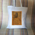 White cotton tote bag: A compact-shaped owl with brown feathers sits sideways on an upright, roughly semi-circular stone arch, while looking directly at the viewer. The arch is decorated with a central circular Celtic knotwork design. A border of ivy leaves and simple curls surrounds the owl and down each side of the arch. The design is mostly monochrome apart from the owl, with a background of mottled dark tan.