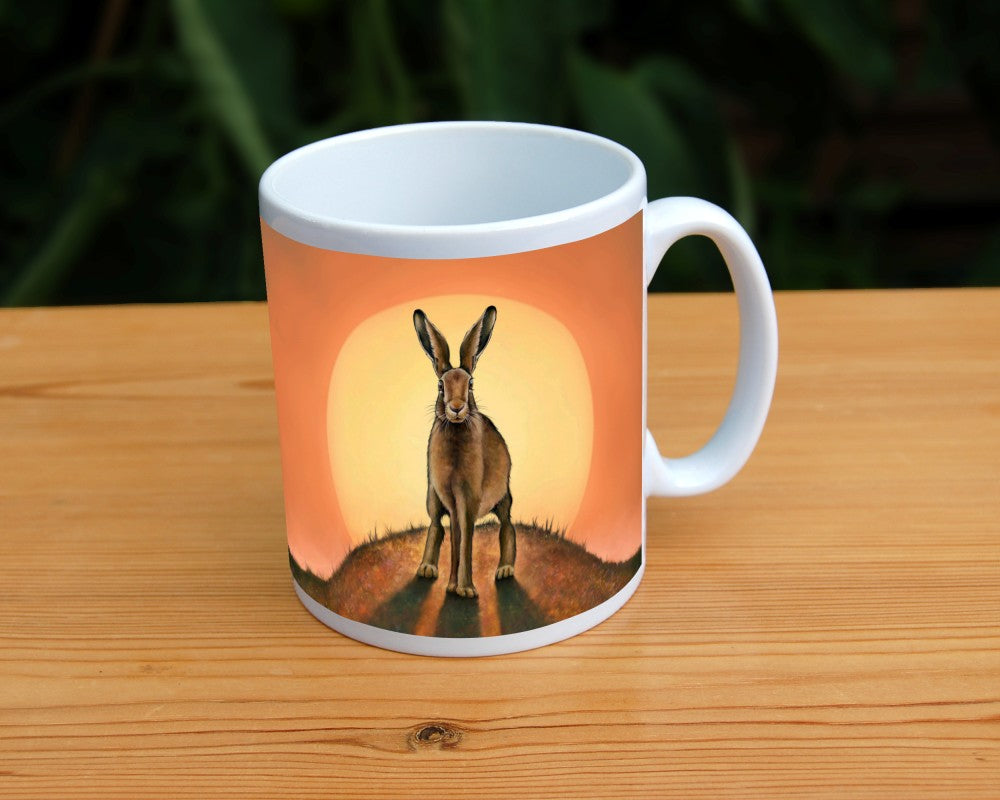 A brown hare stands on top of a small hill facing the viewer. The sun is rising behind the hare. The colours are mostly yellow, orange and brown.