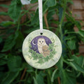Illustration of the head and body of a brown and cream owl, enclosed in a circle with ivy leaves around the bottom two thirds, and a purple night sky with crescent moon and stars in the background. The bird is facing to the left, with its head turned to face the viewer. Stars can be seen in its eyes. The overall background is a mottled green.