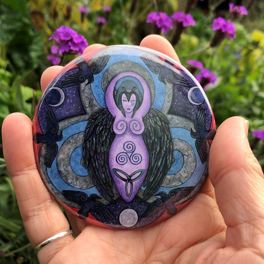 A raven stands behind a purple Goddess figure, its huge wings folded down her sides. She stands in the centre of a ring. Ravens fly around the inside of the ring, with each aspect of the triple moon also present. Colours are purple, red, and blue.