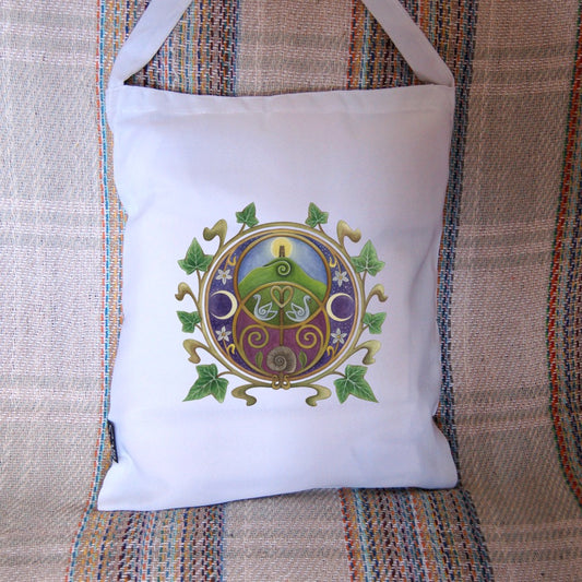 A circular design on a white background featuring the Chalice Well (Vesica Pisces) symbol inside a circle of ivy leaves. Glastonbury Tor, the sun rising behind the tower against a blue sky, nestles inside the upper circle of the symbol, with two swans in the area where the two circles join. An ammonite is inside the lower circle, against a maroon background. To the left and right are two opposing crescent moons, and small white flowers.