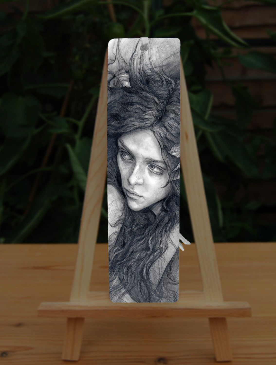 A rectangular bookmark: Pencil illustration of the head and shoulders of a young woman looking back over her shoulder. She has a mass of hair sticking out in all directions around her head and down her front. 