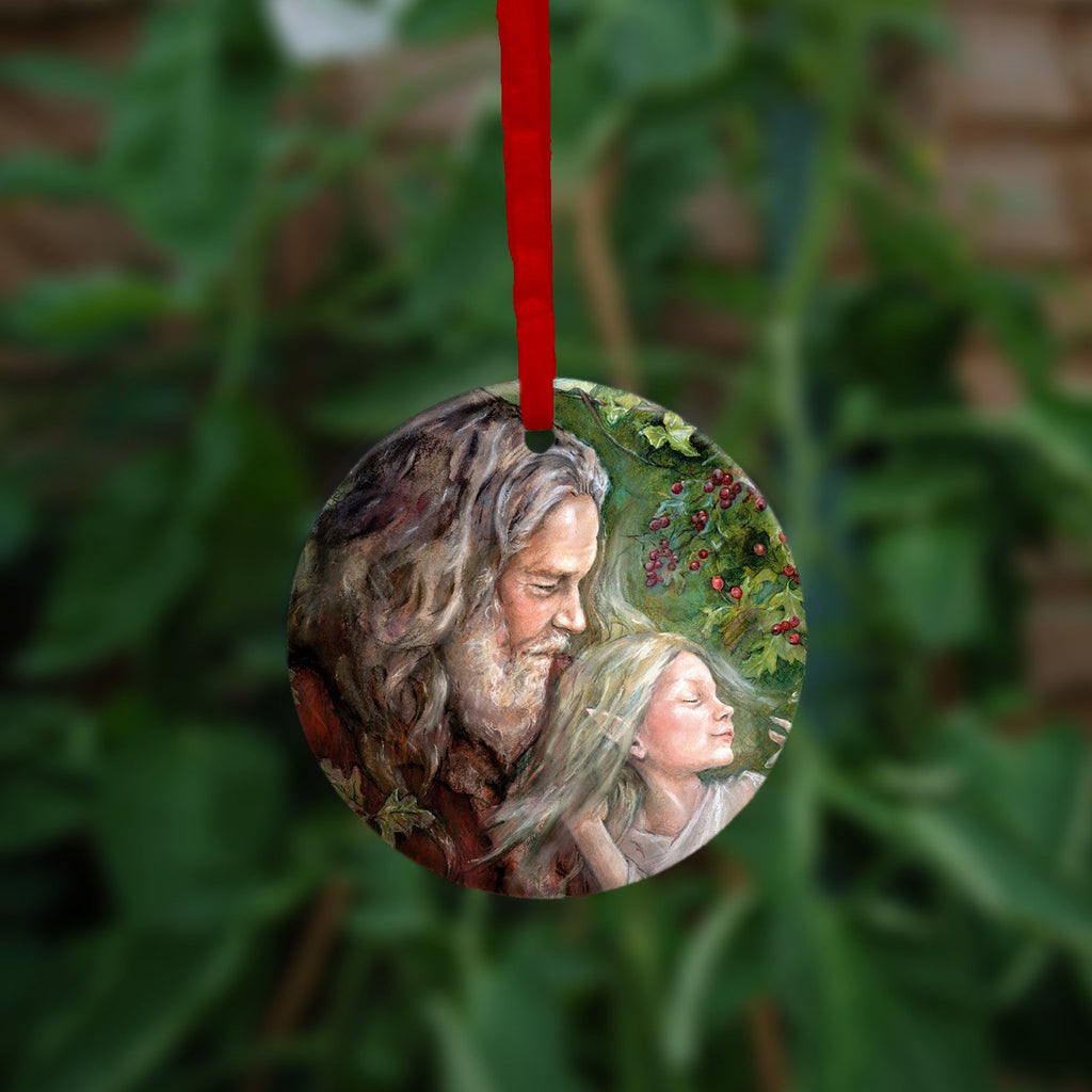 Circular hanging ornament with a red ribbon: An older man with long hair, grey beard, and wearing a red coat cradles a sleeping fairy, wearing a pale gossamer dress, in his arms. Branches of hawthorn and ivy fill the background.