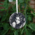 Circular hanging ornament with a white ribbon: Pencil illustration of the head and shoulders of a young woman looking back over her shoulder. She has a mass of hair sticking out in all directions around her head and down her front. Leaves are woven - or perhaps stuck - in her hair.