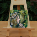 A square coaster: A young woman with a garland of pale flowers in her hair closes her eyes as she moves to kiss a green man.