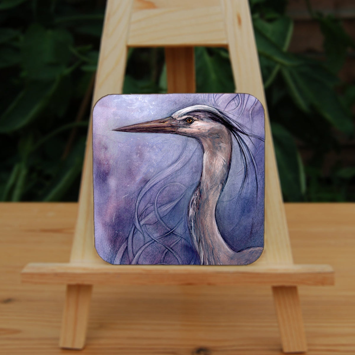 A square coaster: A sideways view of the head and neck of a heron. The background is a mottled purple with a swirl pattern.