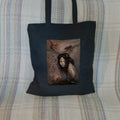 Black tote bag: The head and body of a young woman appears above a thick tree branch, upon which sits a red squirrel. Two more squirrels crouch on a branch above her. The woman is turning her head as if to look behind her. She has long brown hair with leaves stuck in it. Autumnal leaves and branches fill the scene. Colours are reds, oranges and browns.
