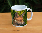 A white ceramic mug: The head and neck of a red fox, their face angled towards the front right. The background consists of swirls of branches and leaves in a rich green colour.