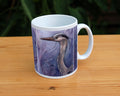 A white ceramic mug: A sideways view of the head and neck of a heron. The background is a mottled purple with a swirl pattern.