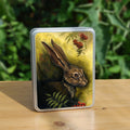 Rectangular metal tin: The head and shoulders of a hare facing to the right. Sprigs of red rowan berries and leaves are drawn above and below. The background is mottled yellows and browns.