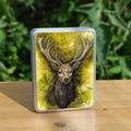 Rectangular metal tin: The head and chest of an antlered stag directly facing the viewer. Oak leaves are drawn to his left and right. The background is mottled yellows and browns.