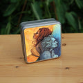 Square metal tin: A painting of two diagonal halves: to the top/left, against a background of mottled orange, a young woman with red hair and orange dress faces to the left. She appears to be leaning against, and blending with, an elderly woman who faces towards the right/bottom in the other half of the design. This half is coloured in shades of blue and grey.