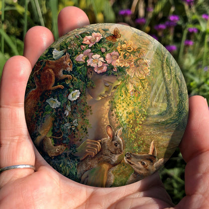 A young woman sits in a forest. Her long hair is made of flowering ivy and covered in flowers including honeysuckle and dog rose. A squirrel clings to one side, a mouse peers upwards toward her, and butterflies hover above. A deer sits to one side and in her arms she holds a rabbit.