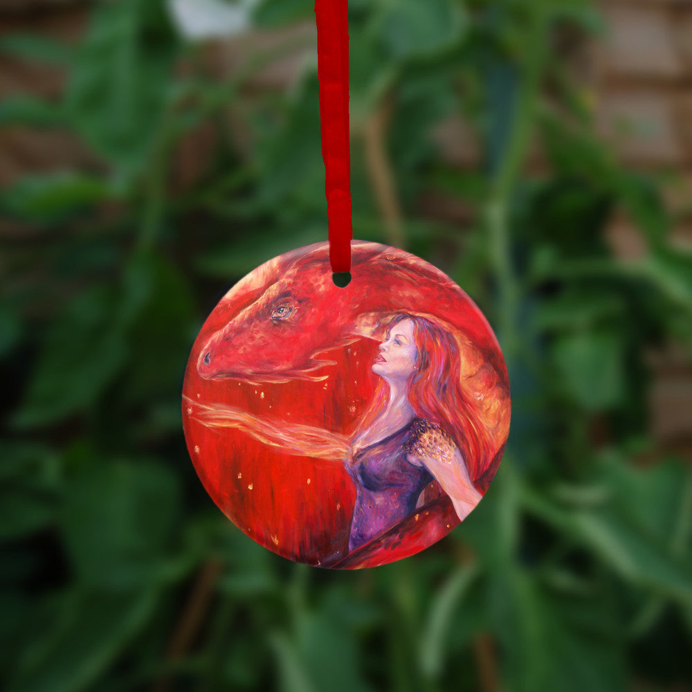 A woman with long red hair and wearing a sleeveless purple dress stands in front of a red dragon. Both look to the left. A wing wraps around one side, with the head on the other. A stream of fire is emitting from the location of the woman's heart. The overall design colour is red.