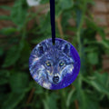 The head of a wolf, looking directly at the viewer. The overall colour of both the wolf and the background are shades of blue, with the exception of yellow/green eyes and flashes of paler fur around the neck.