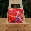 A woman with long red hair and wearing a sleeveless purple dress stands in front of a red dragon. Both look to the left. A wing wraps around one side, with the head on the other. A stream of fire is emitting from the location of the woman's heart. The overall design colour is red.