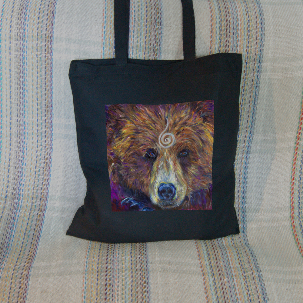 The head of a bear looking directly at the viewer. A pale-coloured spiral is coiled at their forehead, opening upwards. Their fur is a mixture of reds, golds and browns, with a pale snout.