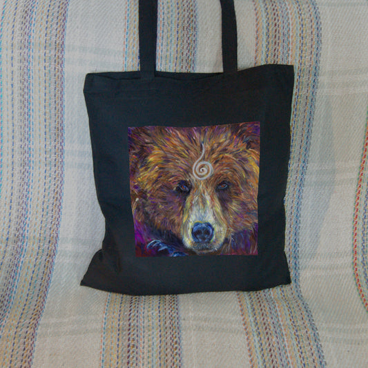 The head of a bear looking directly at the viewer. A pale-coloured spiral is coiled at their forehead, opening upwards. Their fur is a mixture of reds, golds and browns, with a pale snout.