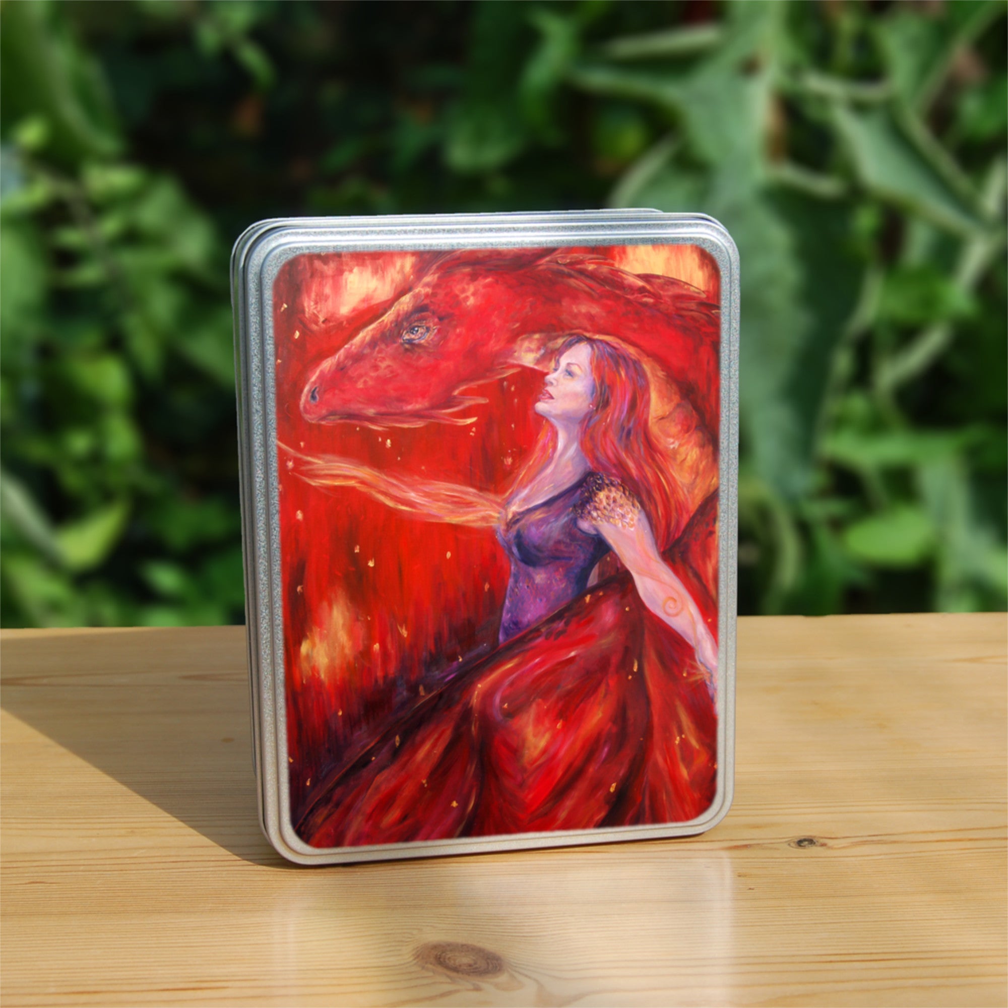 A woman with long red hair and wearing a sleeveless purple dress stands in front of a red dragon. Both look to the left. A wing wraps around one side, with the head on the other. A stream of fire is emitting from the location of the woman's heart. The overall design colour is red.