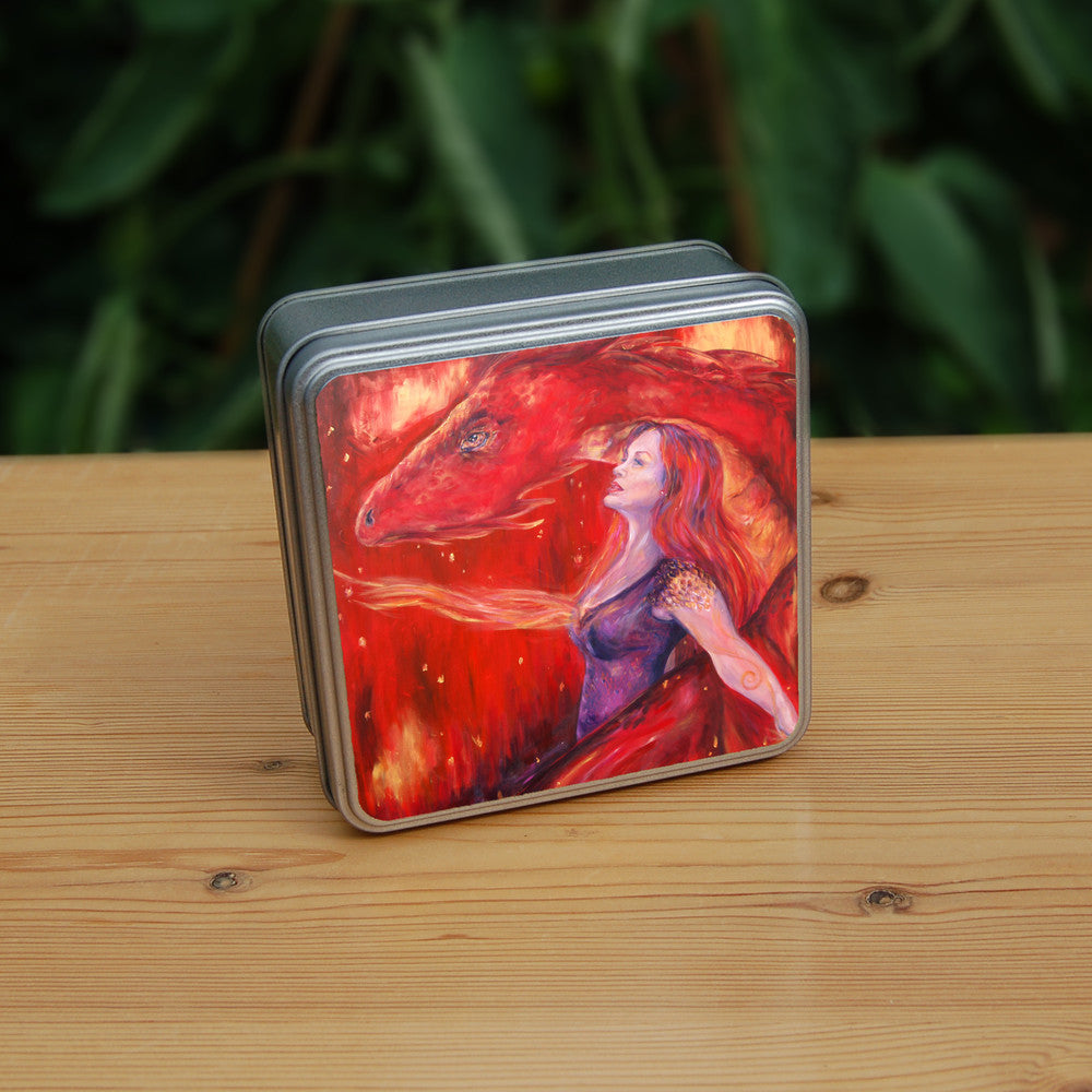 A woman with long red hair and wearing a sleeveless purple dress stands in front of a red dragon. Both look to the left. A wing wraps around one side, with the head on the other. A stream of fire is emitting from the location of the woman's heart. The overall design colour is red.
