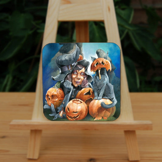 A wide-eyed woman sits up on her elbows, head resting on her hand, her black pointed hat sitting drooping and crooked on her head. She's surrounded by four pumpkins, carved with grotesque faces. A cat sits on one of the pumpkins, the top half of another pumpkin squashed over their head, ears protruding out of the top, and pumpkin juice oozing down their front.