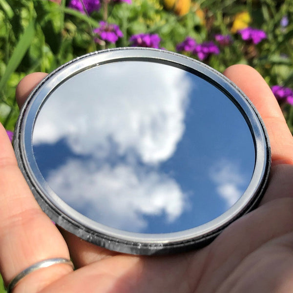 The mirrored side of the pocket mirror. The mirror fills the entire back, except for a small silver border.