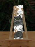 A mass of cats of all colours and in many poses surrounds the face of a red-haired woman with cat-slit eyes and ears, and a Eye of Horus symbol on her forehead. A white cat sits on her head. Colours are oranges, reds, black and white.