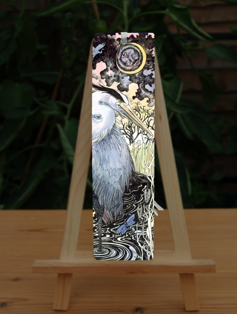 A large grey and white heron stands on one leg in water near the bank of a river. A damselfly hovers nearby. Runes (Berkana and Algiz) dangle from the heron's beak. The river extends behind the scene, with grassland and trees beyond. An unborn human baby lies curled up within the sun.