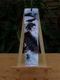A pencil drawing. A large back raven wing flows into the head and neck of a figure with with sharp facial features, pointed ears and black raven-feather hair. A raven sits on the head of the figure. The design is colour-washed in purple.