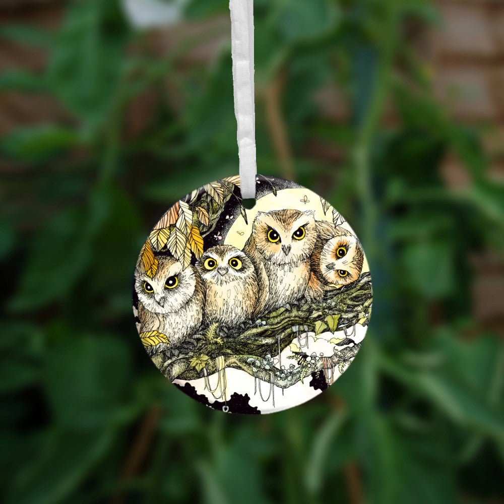 Four owls sit on the branch of a tree looking towards the viewer. One owl at the end has his head tilted sideways. Brown leaves splay down from above and a full moon shines behind them. Clouties and other offerings are wrapped around a branch below them.