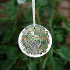 The other side of the ornament. A flower-filled meadow. A stag and badger stand either side, and a hare, blackbird, mouse, and other creatures are nestled within. The head and shoulders of a young woman lying on her back rise from the ground. Beneath her, the bottom half of the oval is a mass of twisting roots, branches, leaves, fungi and toadstools. A snake winds its way through the top half with its head appearing at the bottom.