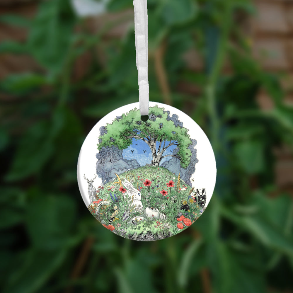 One side of the ornament. At the top there's a tree in full leaf, surrounded by clouds, but clearing to blue in the centre, and swifts wheeling all around. Beneath, the top half of the oval is a flower-filled meadow. A stag and badger stand either side, and a hare, blackbird, mouse, and other creatures are nestled within. The head and shoulders of a young woman lying on her back rise from the ground. 