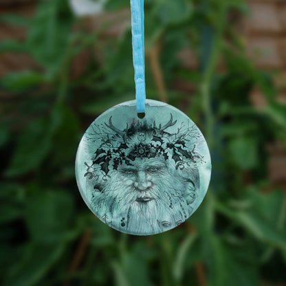 An outline pencil drawing of an old man with a beard facing the viewer. Small antlers sit above, and sprigs of holly surround the upper half of his face. Two small faces, facing outwards, appear from either side of his beard. A young elven face peers through bottom right.  The design is colour-washed in green.