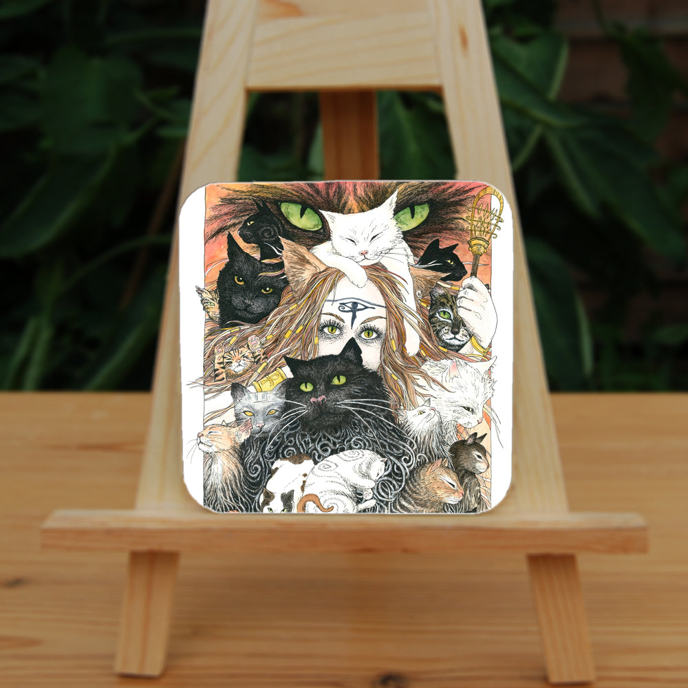 A mass of cats of all colours and in many poses surrounds the face of a red-haired woman with cat-slit eyes and ears, and a Eye of Horus symbol on her forehead. A white cat sits on her head. She holds a gold-coloured sistrum (a type of rattle) in one hand. The head of a much larger cat with green eyes appears above and behind them. Colours are oranges, reds, black and white.