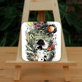 A figure in white with black hair is curled up in the foetal position above a yin-yang symbol. A second smaller figure in black with white hair lies above her. A multitude of plants and flowers surround them, rising upwards towards a sun and moon to the left and right, and red echinacea flowers in the centre.