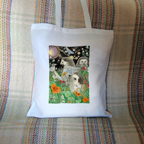 It's night-time and three hedgehogs are playing in a flowerbed. One sits amongst orange and red blooms. Behind him, one is climbing out of a large watering can and another peers over an upturned flower pot. Blue moths sit on the watering can and flitter overhead. A full moon shines in the night sky.