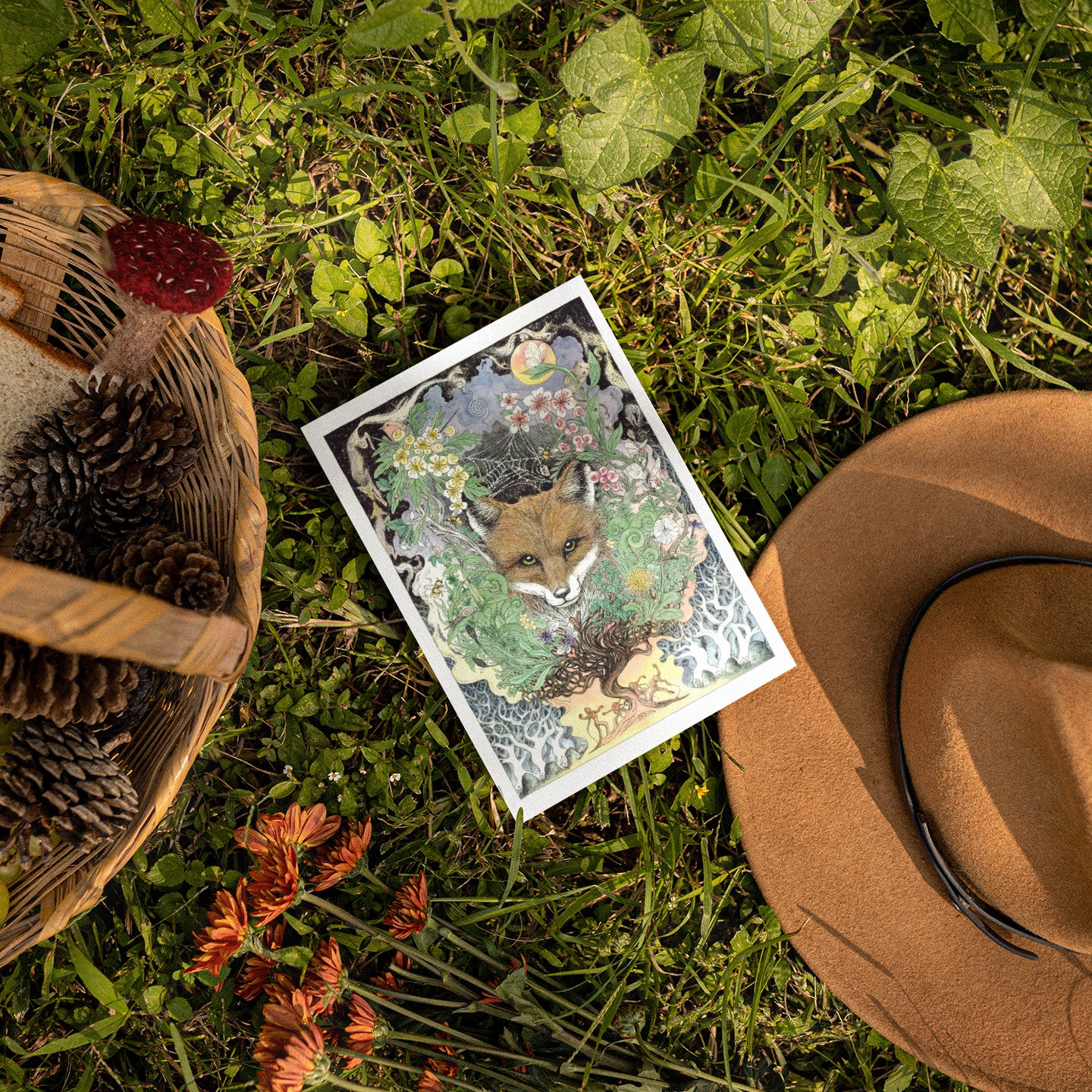 Card with a fox design on grass next to a hat and basket