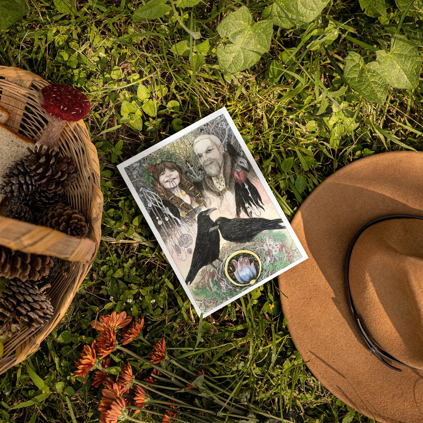 Card with a mystical design of a man, woman, and raven on grass with a hat and basket.