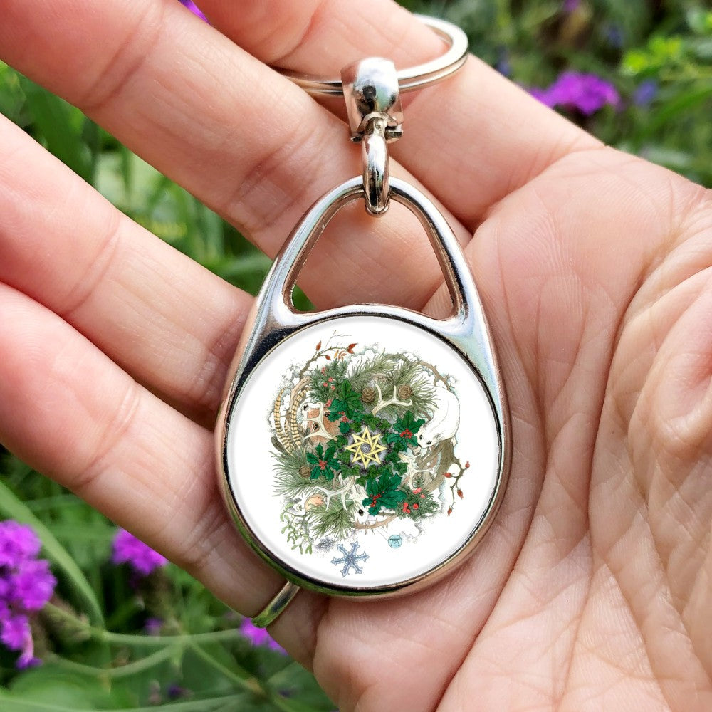 A central eight-pointed star sits within a wreath of ivy. Clusters of berried holly are interspersed with pine fronds and cones, and antlers. A white stoat, white hare, robin and fox appear around the fronds and standing on an outer circle of thorny rose-hipped branches. A single snowflake falls below. Yew and mistletoe also feature.