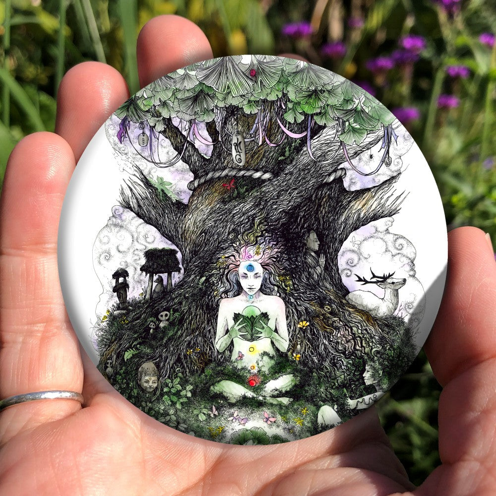 A human figure sits cross-legged at the bottom of a large Ginkgo tree, holding a Ginkgo seed in a nest of leaves in their hands. Chakra positions are marked in colour on the figure, and their hair flows out to become part of the tree. Clooties hang from the tree. A white stag sits to the right.