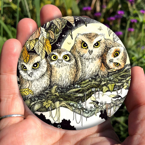 Four owls sit on the branch of a tree looking towards the viewer. One owl at the end has his head tilted sideways. Brown leaves splay down from above and a full moon shines behind them. Clouties and other offerings are wrapped around a branch below them.
