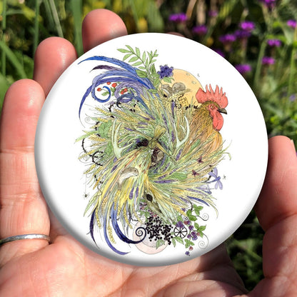 A cockerel with swirling blue, green and yellow/orange feathers, also incorporating leaves and wheat ears. Mice nibble on the ears, and butterflies and dragonflies flutter and swoop around. At the bottom, a crescent moon peeks from behind sprigs of berries. A yellow sun appears behind the head of the cockerel. A corn dolly is formed in the centre of the swirl of feathers, and a mouse sits in its skirt.